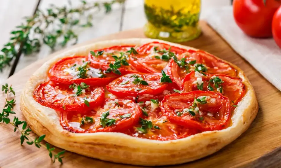 Tarte aux tomates cerises, garnie d'herbes fraîches et d'ail, prête à être dégustée.