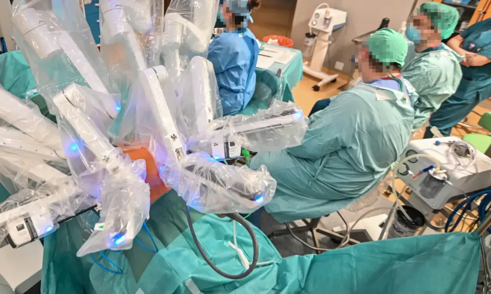 Chirurdzy w zielonych fartuchach prowadzą operację prostaty da Vinci. Robotyczne ramiona systemu są widoczne, pokryte sterylnymi osłonami.