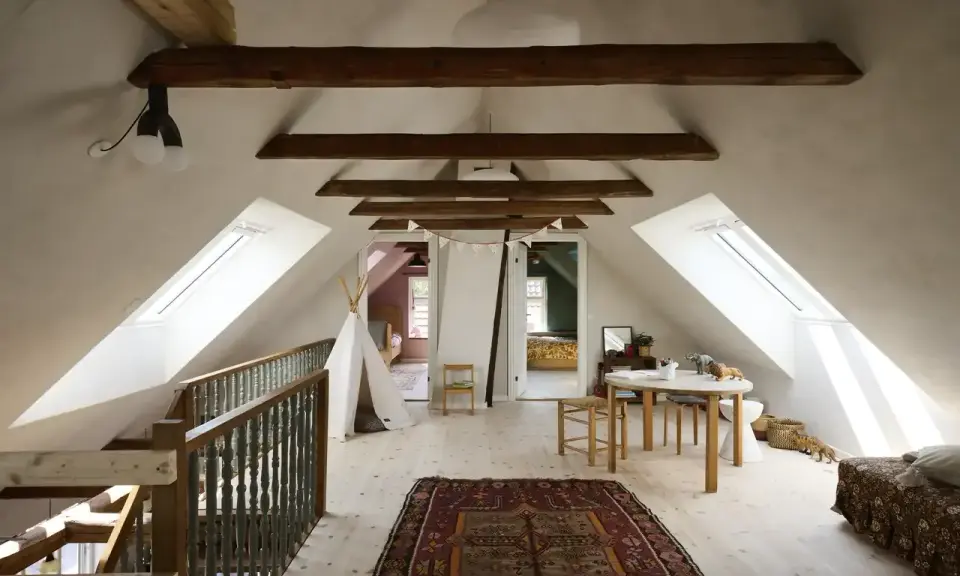 Idee per ristrutturare casa antica: mansarda luminosa con travi a vista, tappeto persiano, teepee e tavolino per bambini.
