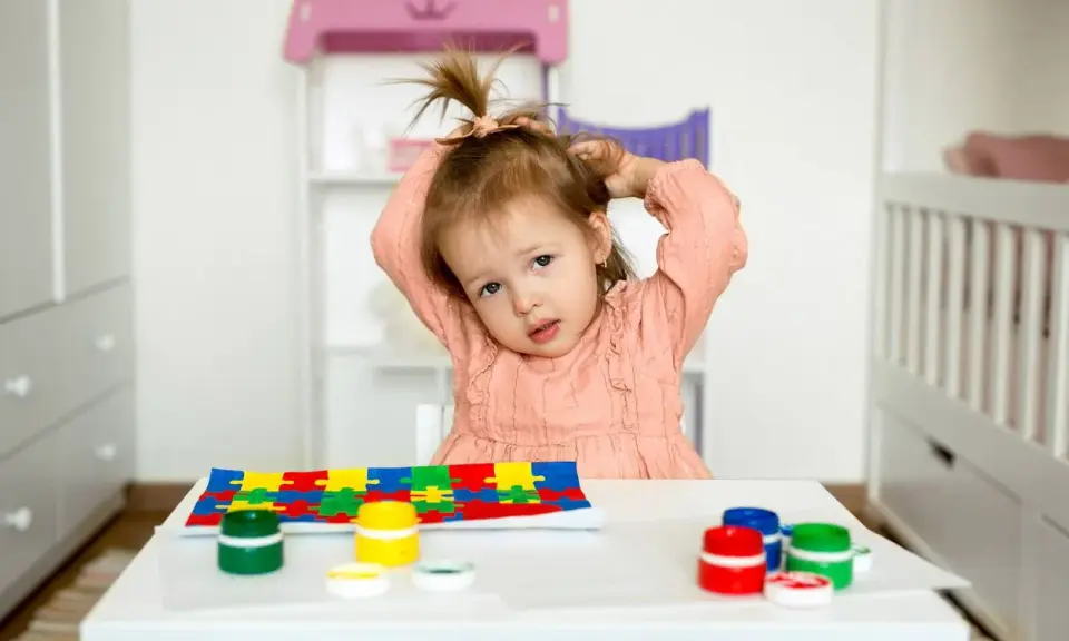 Bambina con puzzle e colori, un'immagine che fa riflettere su cos'è l'asperger e come supportare i bambini.