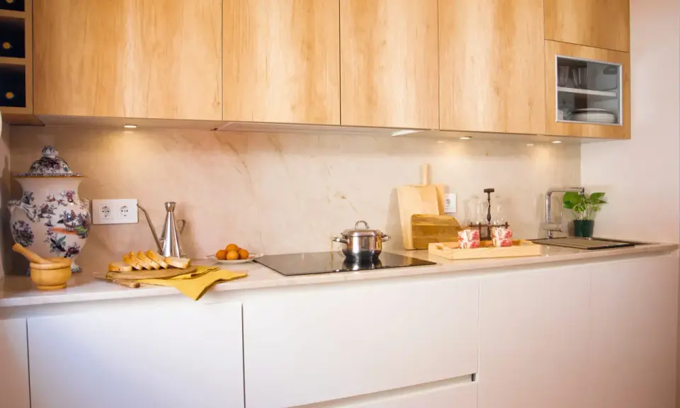 Cocina blanca y madera con encimera de mármol. Hay pan, huevos, una olla y una planta.