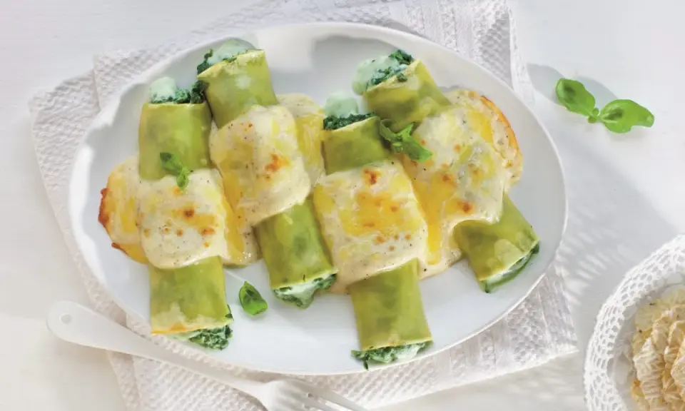 Pyszne cannelloni ze szpinakiem, zapieczone pod kremowym sosem serowym, ozdobione listkami bazylii.