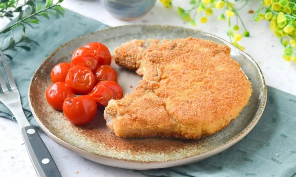 Cotoletta alla milanese dorada y crujiente, acompañada de tomates cherry asados. Un plato clásico y delicioso.