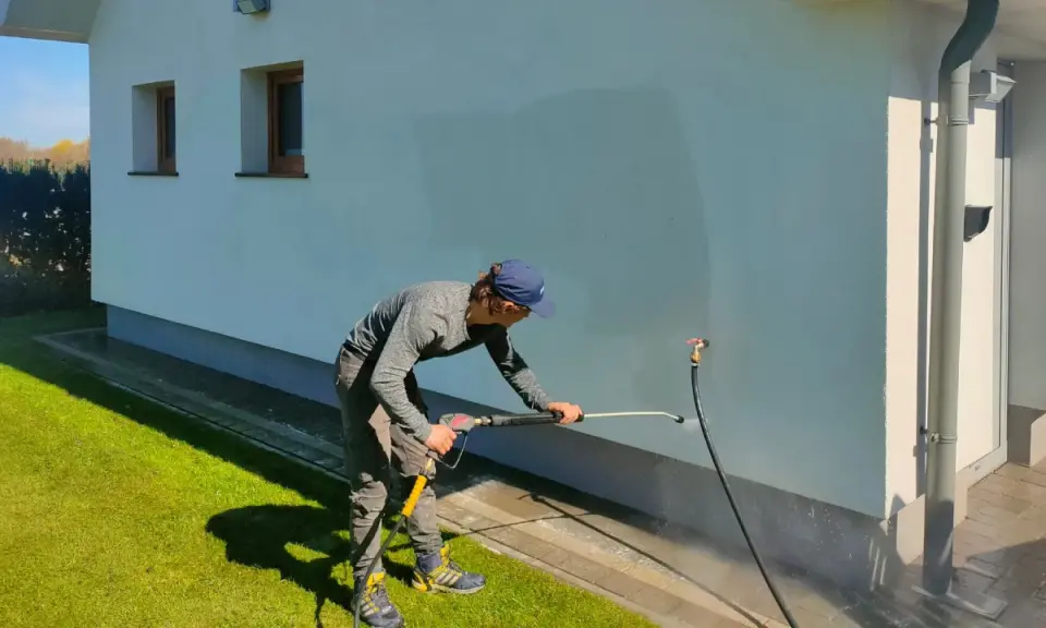 Mężczyzna myje elewację domu myjką ciśnieniową.