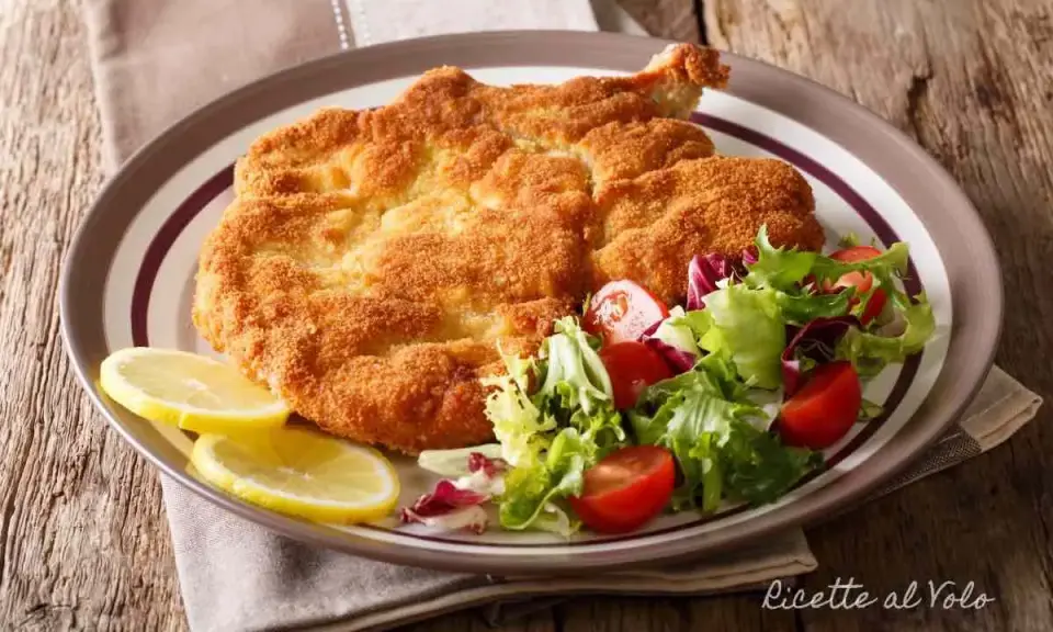 Cotoletta alla milanese dorata e croccante, servita con insalata fresca e spicchi di limone.