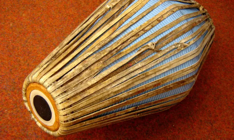 Mridanga, jeden z najstarszych instrumentów muzycznych, z niebieską membraną i drewnianymi wzmocnieniami, leży na pomarańczowym tle.