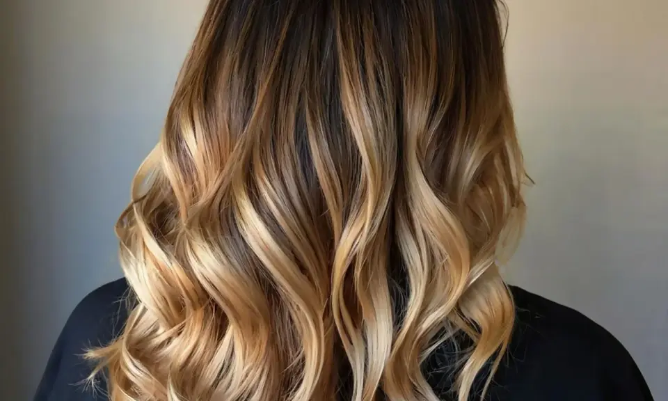 Piękne, falowane włosy z subtelnymi refleksami blond na ciemnych włosach, tworzące efekt ombre.