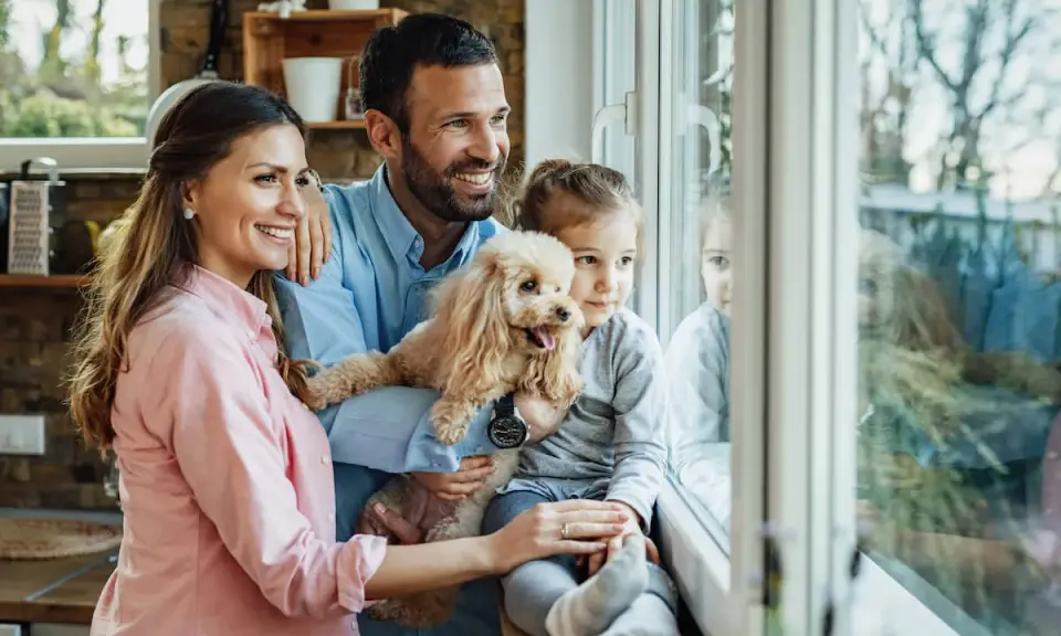 Szczęśliwa rodzina zastępcza, z pieskiem w ramionach, patrzy przez okno. Marzą o adopcji i wspólnym życiu.