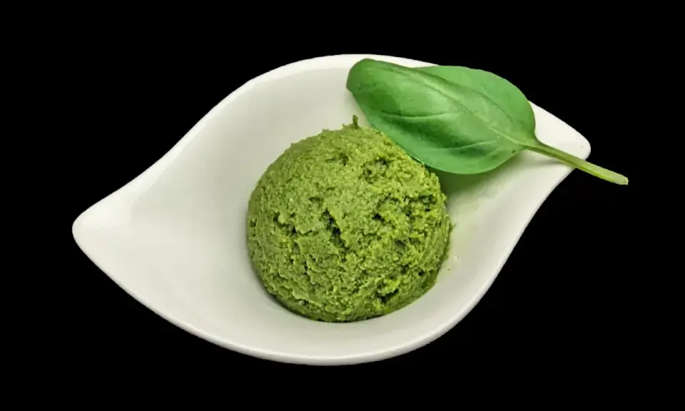Une cuillère de pesto maison, d'un vert vibrant, garnie d'une feuille de basilic frais, dans une coupelle blanche.