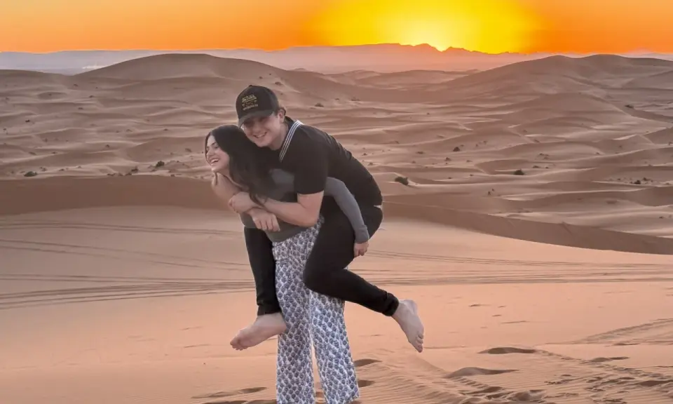 Jóvenes disfrutando de un atardecer en las dunas de Marruecos con niños.
