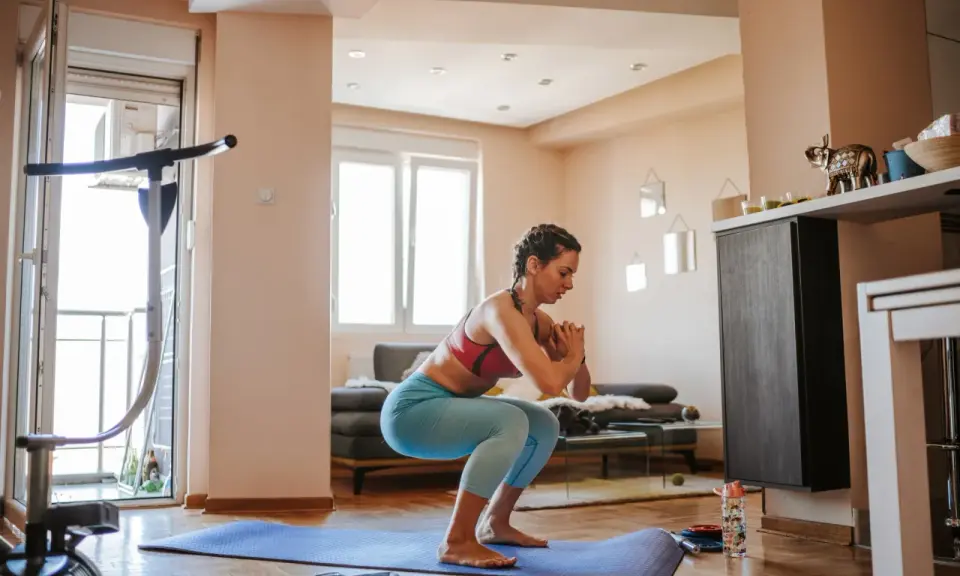 Frau macht Kniebeugen auf einer Matte, ein Beispiel für effektives **Eigengewicht Training** zu Hause.