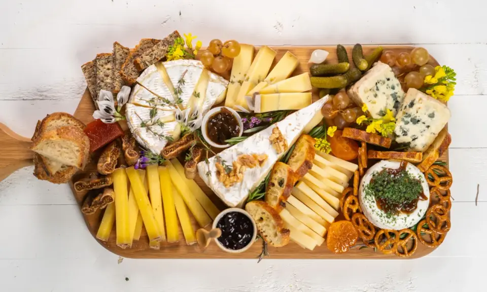 Una tabla de quesos sencilla con variedad de quesos, pan, frutas secas, uvas, pepinillos y mermelada.