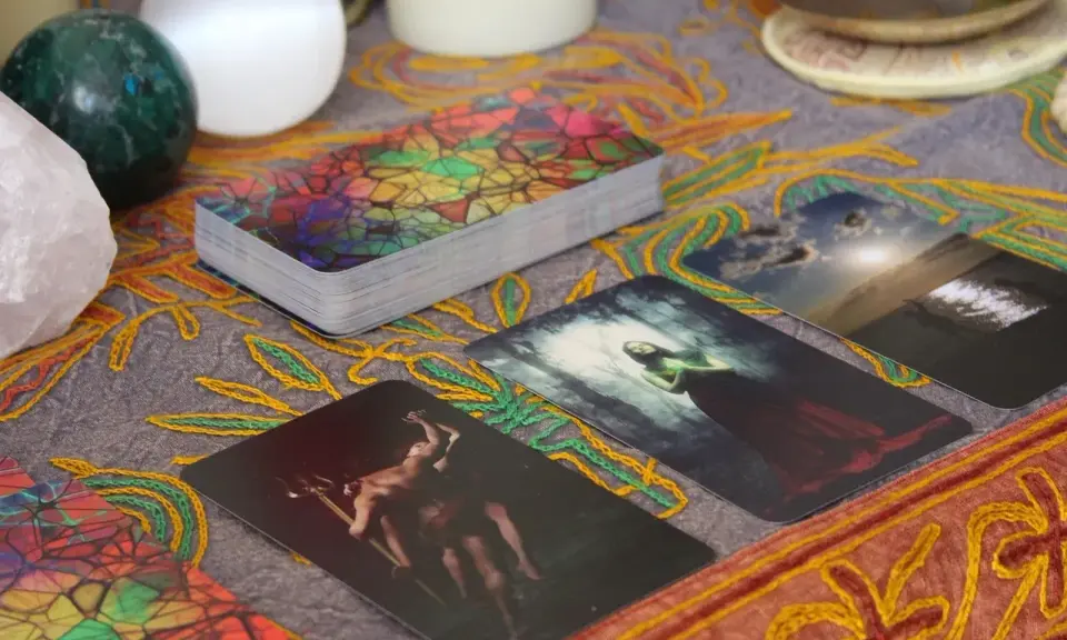 Tarot dzienny ryby: karty z mistycznymi obrazami, kryształ, kule i ozdobny obrus tworzą atmosferę wróżenia.
