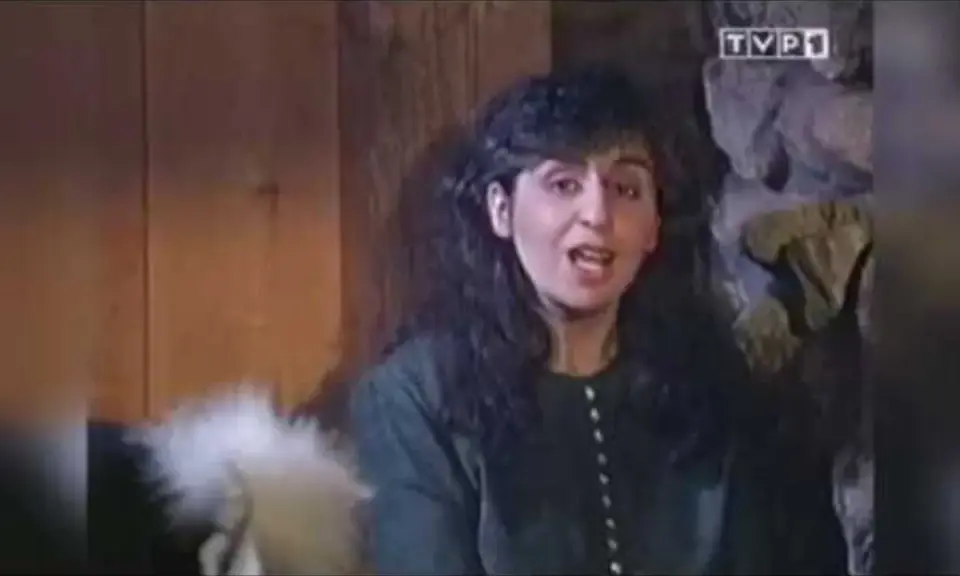 Kobieta z ciemnymi włosami, w zielonej bluzce, mówi do kamery. Chciałabym być tam gdzie ty, w tym przytulnym wnętrzu.