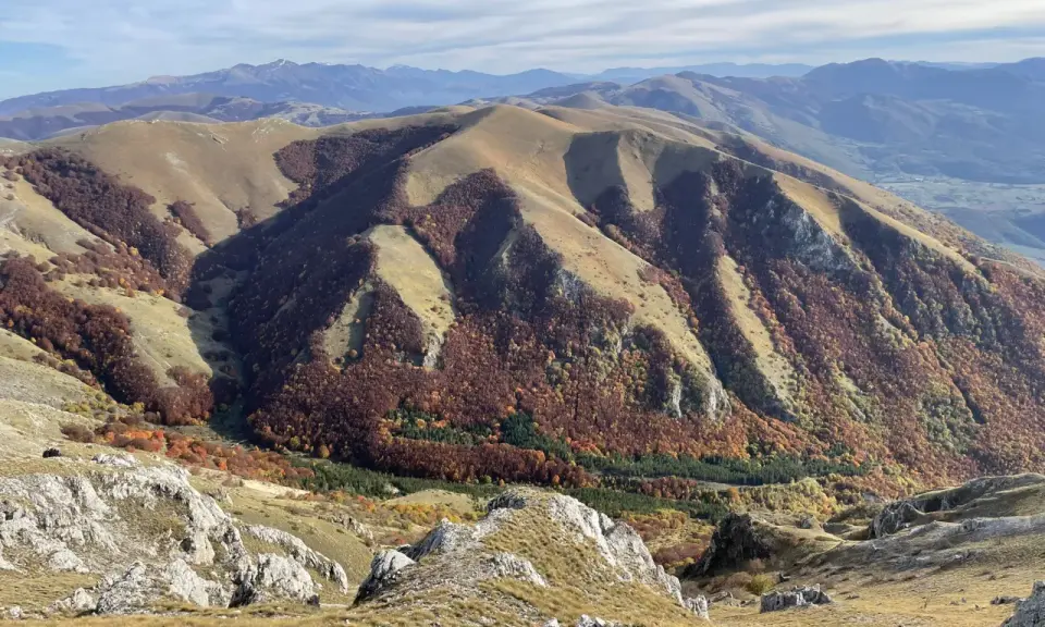 Autunno nel Val di Norcia, con montagne dolci e boschi dai colori caldi che scendono verso la valle.