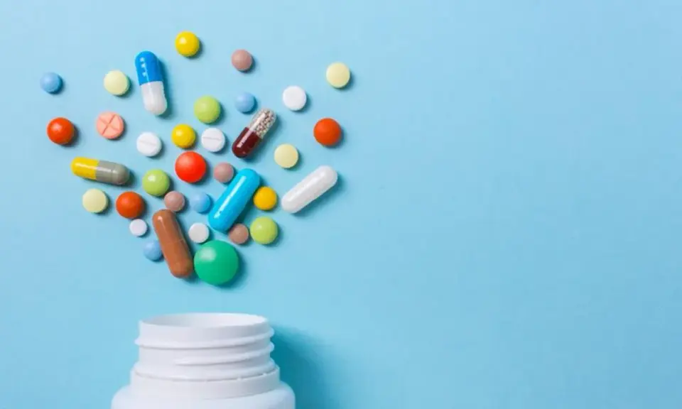 Różnorodne tabletki i kapsułki wysypujące się z białego pojemnika. Czy to opioidy, co to za leki?