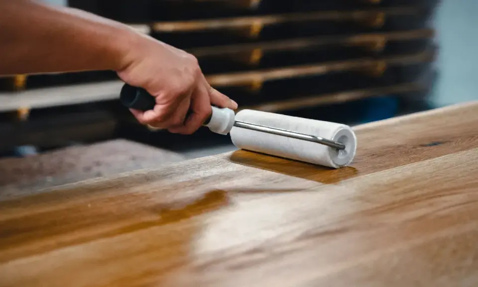Main d'artisan appliquant une couche de vernis sur une table en bois avec un rouleau, pour la protéger et la sublimer.