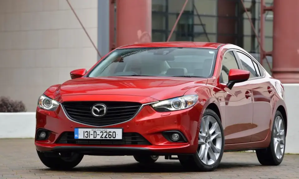 Czerwona Mazda 6, reprezentantka klasy D samochodów, prezentuje się elegancko na tle nowoczesnej architektury.