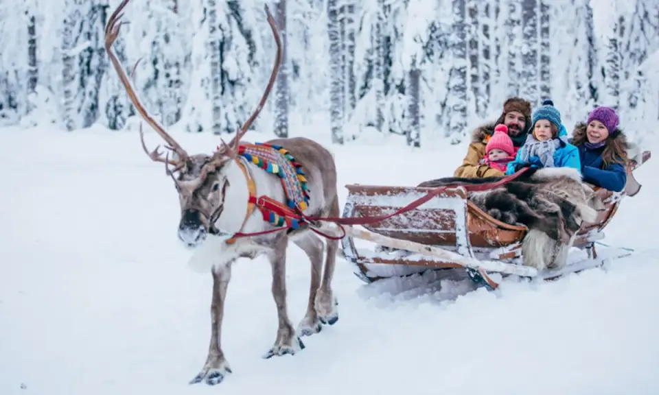 Familie im Rentierschlitten im verschneiten Wald, ein magischer Ausflug im Weihnachtsmann-Dorf Finnland.