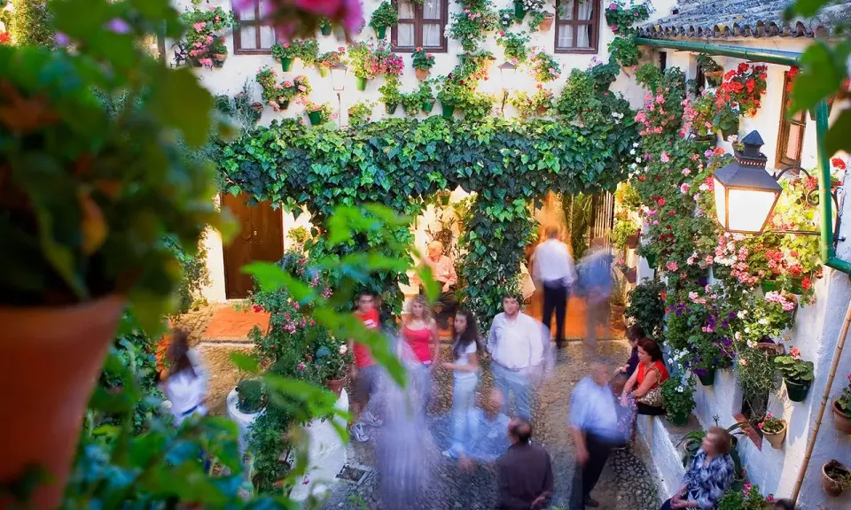 Blühende patios in Córdoba, mit Menschen, die durch den üppig begrünten Innenhof schlendern.