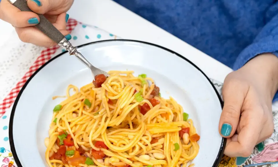 Pyszny obiad bez mięsa: spaghetti z pomidorami, fasolką i szczypiorkiem na talerzu.
