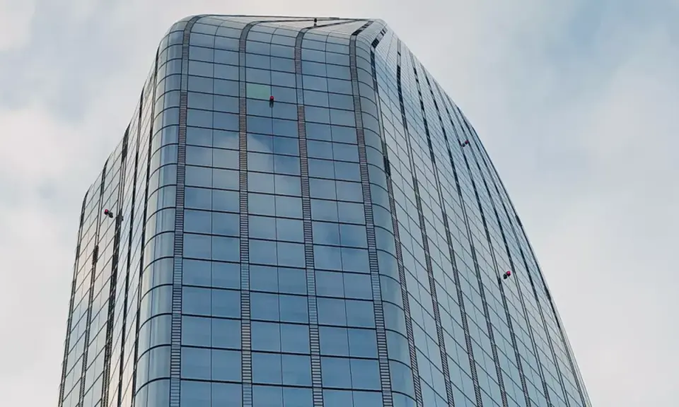 Trabajadores en altura limpian ventanas de edificio moderno. Sikaflex para que sirve: sellar y unir, asegurando la integridad de estas estructuras.