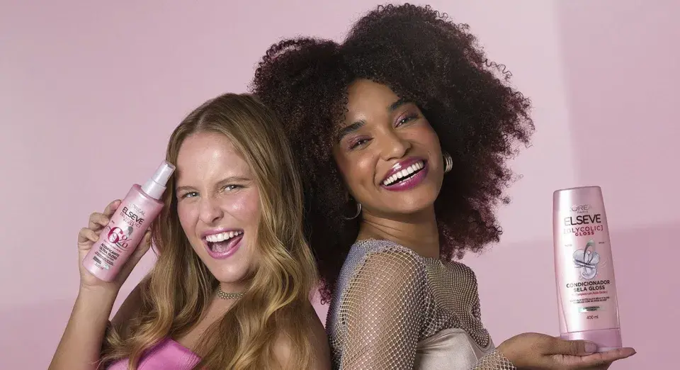 Dos mujeres sonríen, una con pelo liso y otra con pelo esponja, ambas sostienen productos Elseve para un brillo espectacular.