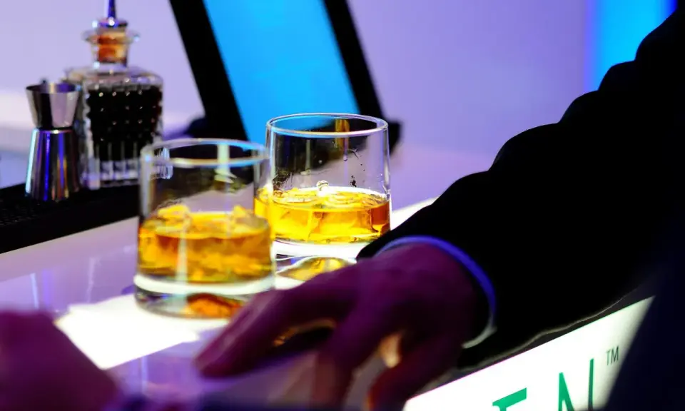 Dwa kieliszki złocistej whisky na barze, idealne na dzień whisky. Dłoń w garniturze sięga po drinka.