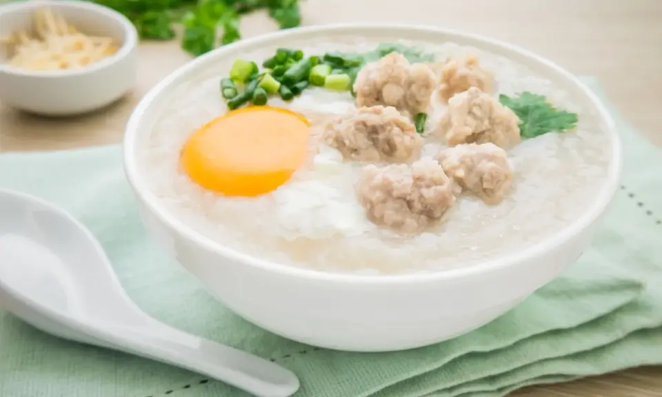 Miseczka aromatycznego congee z mięsnymi klopsikami, jajkiem i szczypiorkiem.