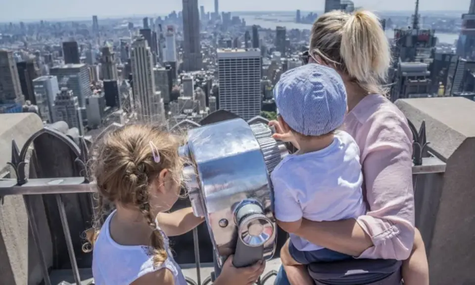 Familia disfrutando de las vistas de Nueva York con niños, explorando la ciudad a través de un telescopio.