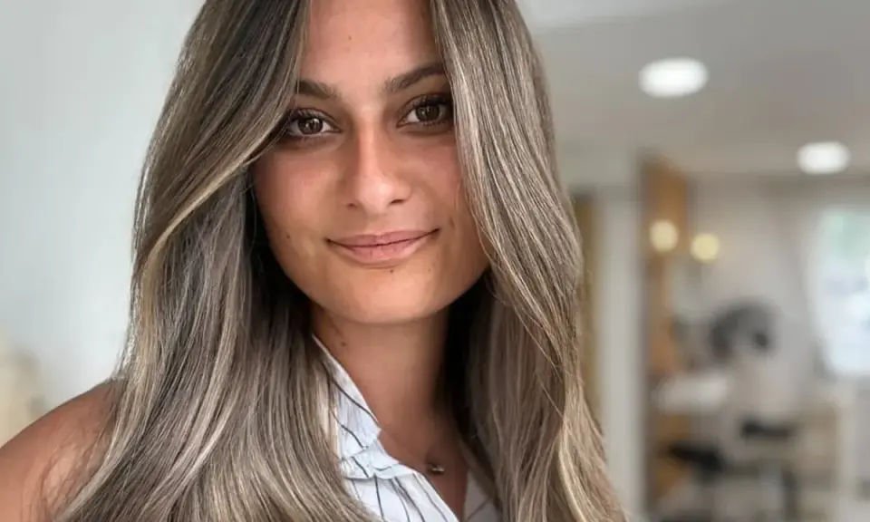 Frau mit langen, welligen Haaren in Balayage-Optik, aschblond mit helleren Strähnen. Ihr Blick ist warm und einladend.