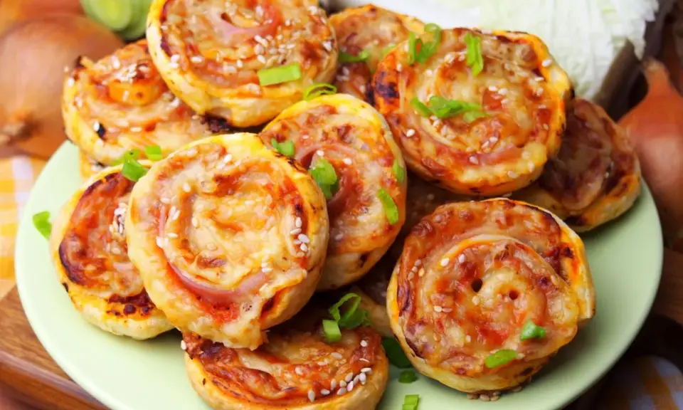 Pyszne pizzerinki z ciasta francuskiego, posypane sezamem i szczypiorkiem, ułożone na talerzu.