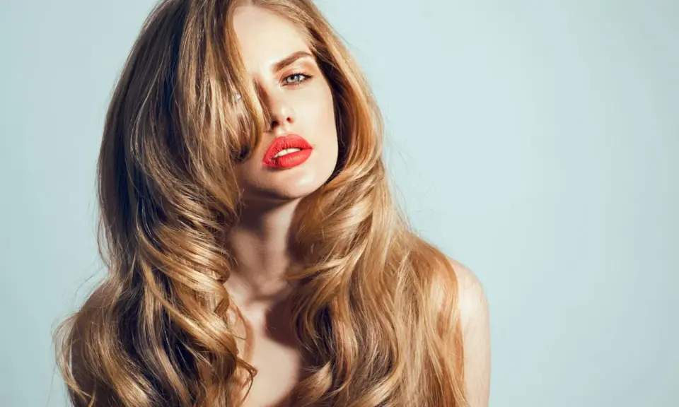 Kobieta z burzą falujących, blond włosów w stylu wolf cut, z wyrazistą czerwoną szminką.