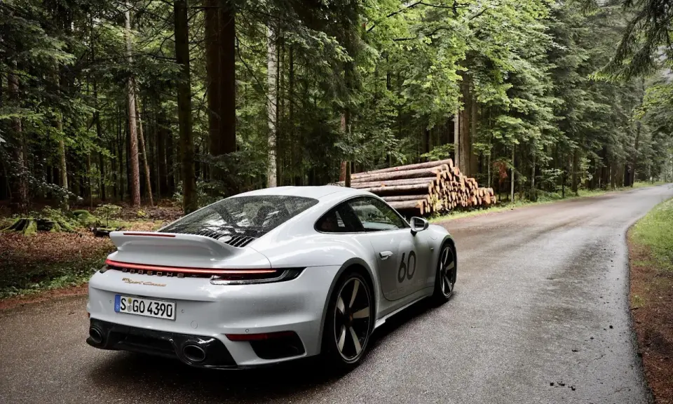 Ein weißer Porsche 911 mit der Nummer 60 auf der Seite fährt auf einer nassen Waldstraße. Die Beschleunigung von 0 auf 100 km/h ist beeindruckend.