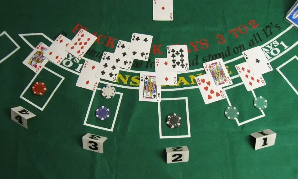 Stół do gry w blackjacka, karty i żetony. Widać karty z numerami i figurami, a także napisy "BLACKJACKS 3 TO 2" i "stand on all 17's".