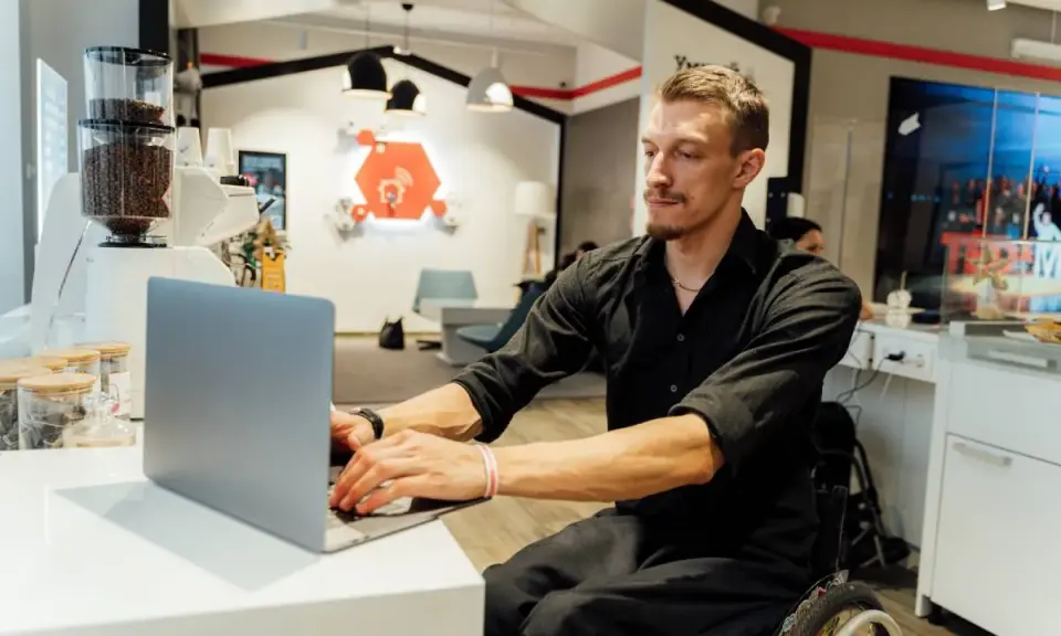 Mężczyzna na wózku inwalidzkim pracuje przy laptopie. To przykład integracji i pracy z grupą inwalidzką.