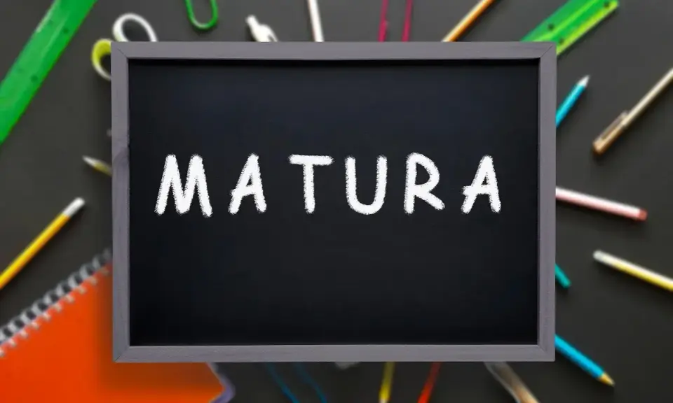 Czarna tablica z napisem "MATURA" kredą, otoczona przyborami szkolnymi. To symbol ważnego świadectwa dojrzałości.