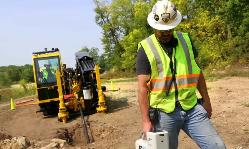 Trabajador supervisa una perforación horizontal dirigida con equipo especializado en un sitio de construcción.