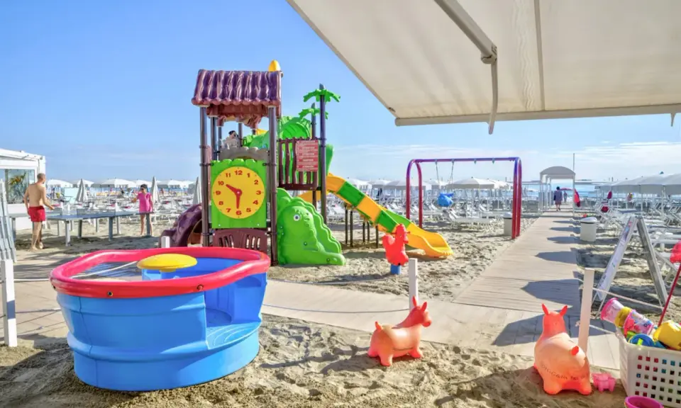 Area giochi su sabbia con scivolo, altalena e giochi d'acqua, un vero lido per bambini.