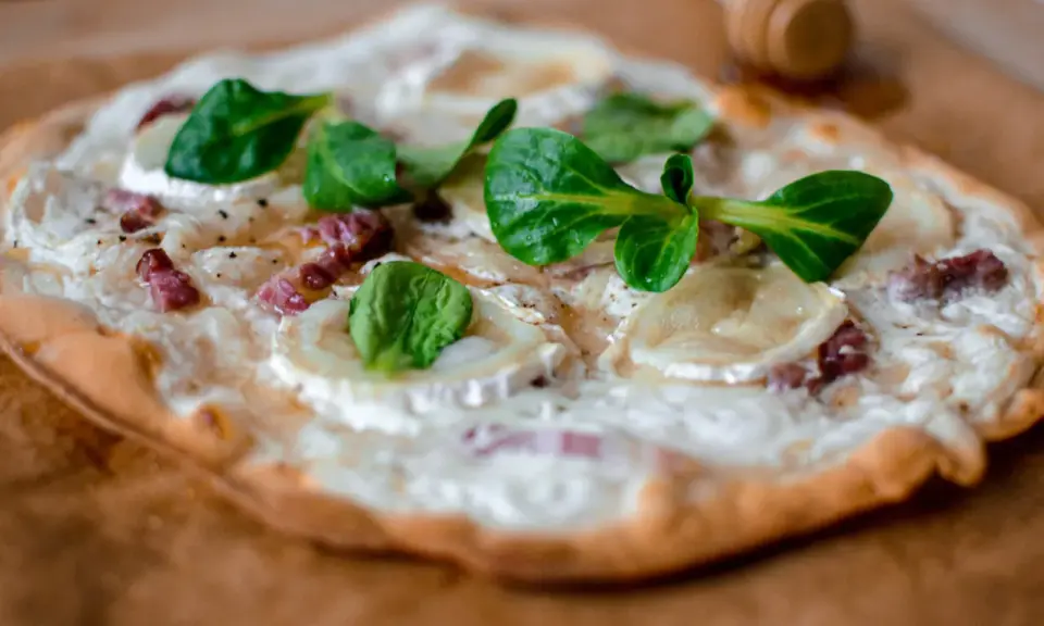 Tarte flambée alsacienne garnie de lardons, fromage de chèvre et jeunes pousses.