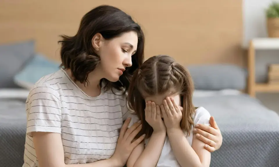 Eine Mutter tröstet ihr weinendes Kind, das sich die Augen zuhält. Möglicherweise kämpft das Kind mit Zwangsgedanken bei Kindern.