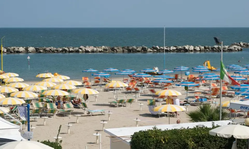 Spiaggia affollata con ombrelloni gialli e bianchi, lettini e il mare azzurro. Un'immagine di igea marittima, perfetta per una vacanza.