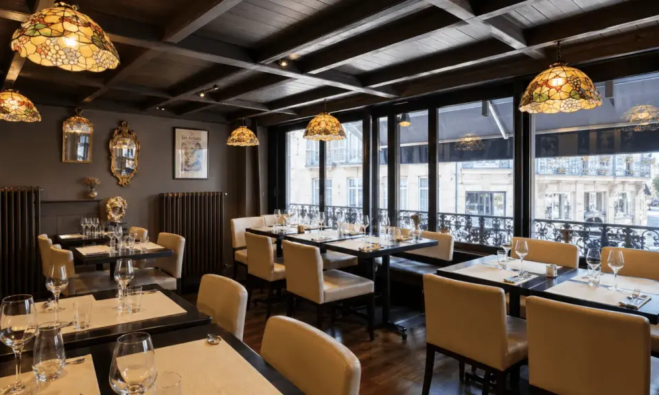 Salle à manger élégante avec des tables dressées, des luminaires Tiffany et une affiche "Les Artistes Limoges Menu" au mur.