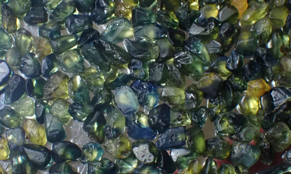 Un mucchio di zaffiri grezzi australiani, con sfumature verdi, blu e gialle. Il loro valore è legato alla rarità e alla bellezza di queste gemme naturali.