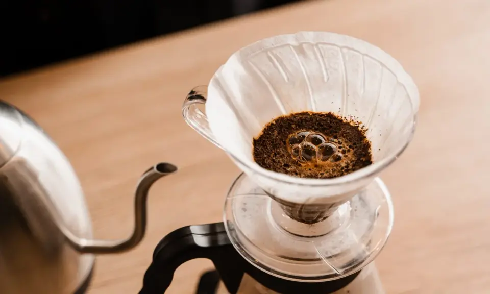 Frisch aufgebrühter Kaffee blubbert im Papierfilter. Ein Wasserkocher steht bereit, um das Ritual des Kaffeefilter selber machen zu beginnen.