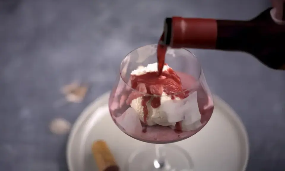 En flaska häller upp rött dessertvin till glass i ett glas. En perfekt kombination för en lyxig efterrätt.