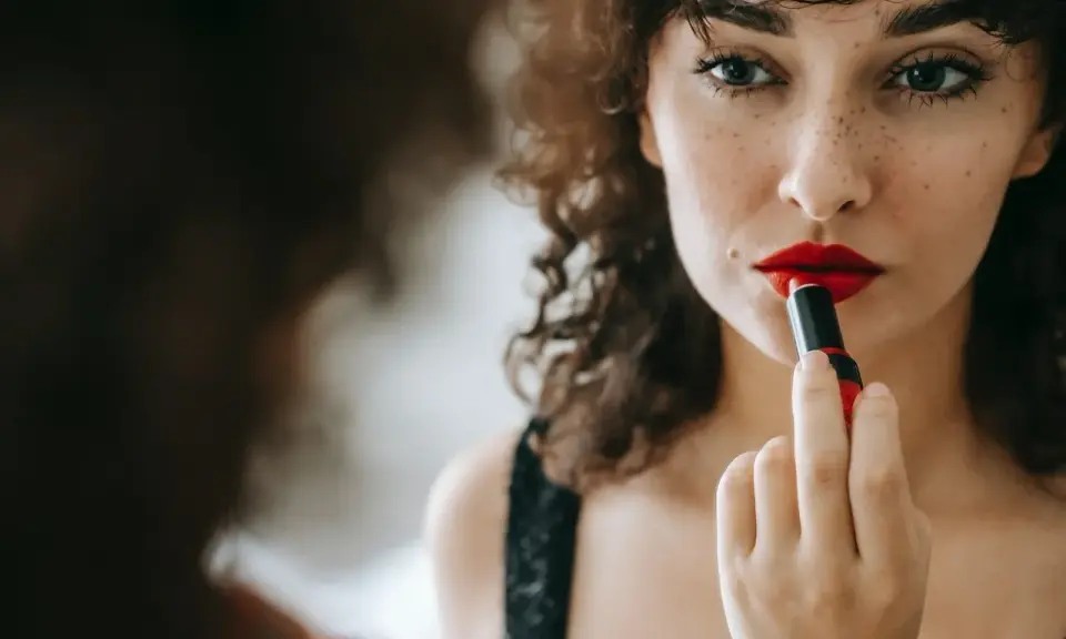 Donna con capelli ricci applica un trucco con rossetto rosso vibrante, creando un look audace e seducente.