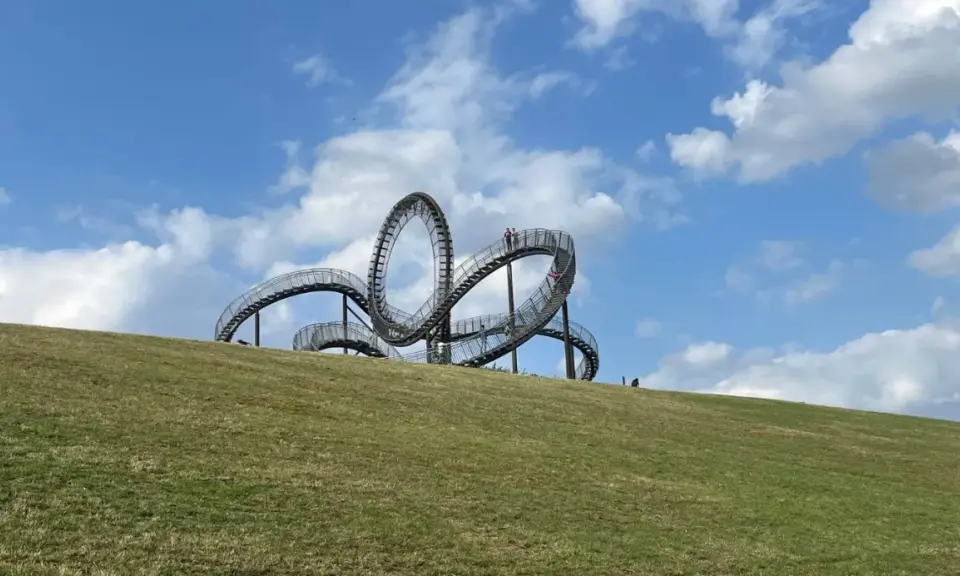 Ein skulpturales Kunstwerk auf einem Hügel, das an eine Achterbahn erinnert. Perfekt für spannende Ausflugsziele mit Kindern.