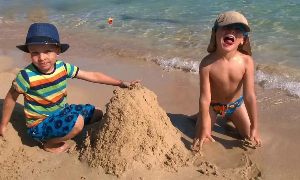Bambini felici in vacanza in Puglia, costruiscono un castello di sabbia sulla spiaggia con il mare cristallino sullo sfondo.