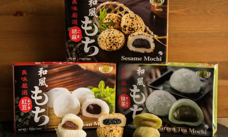 Verschiedene Sorten japanischer Reiskuchen (Mochi) mit Sesam, roter Bohne und grünem Tee, auf dunklem Untergrund vor Holz.